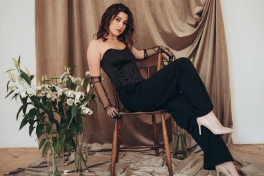 Siyah elbiseli bir kadın çiçek aksanıyla sandalyeye uzanıyor.