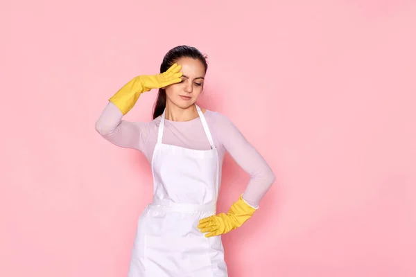 tired woman in gloves and cleaner apron on pink background