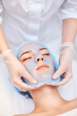 Güzellik uzmanı kaplıcadaki güzel kadının yüzündeki mavi aljinat maskesini çıkarıyor. spa tedavileri