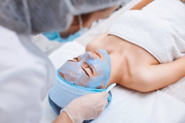 Güzellik uzmanı kaplıcadaki güzel kadının yüzüne mavi aljinat maske takıyor. spa tedavileri