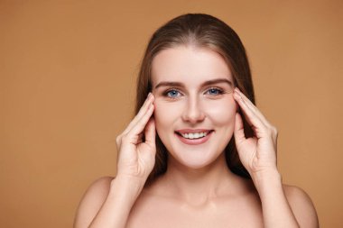 Güzel bir kadın, uzun saçlı ve mükemmel temiz tenli. Bej arka planda yüze dokunuyor.