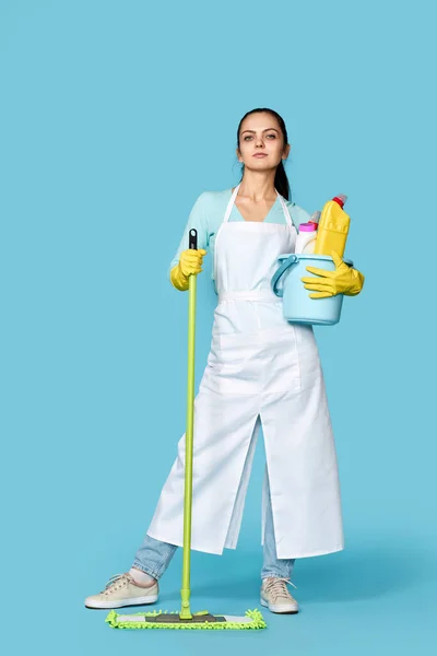 ゴム手袋のきれいなエプロンのきれいな女性青の背景に掃除用品やモップ — ストック写真
