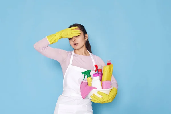 stock image tired caucasian woman in gloves holding bucket with cleaning supplies on blue background.