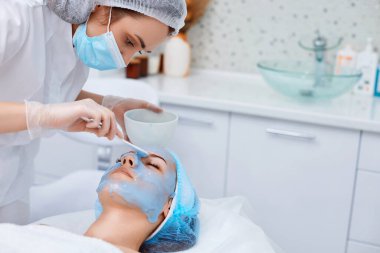 Güzellik uzmanı kaplıcadaki güzel kadının yüzüne mavi aljinat maske takıyor. spa tedavileri
