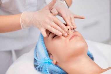 Genç ve güzel bir kadın spa salonunda stres önleyici yüz masajı yaptırıyor.