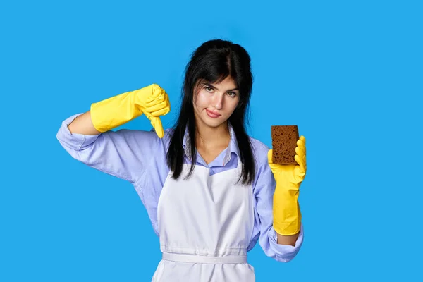 woman in yellow gloves and cleaner apron with sponge showing rejection and negative with thumbs down gesture
