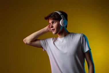 Sarı arka planda kablosuz kulaklıkla müzik dinleyen yakışıklı bir adam. Neon ışıkları