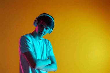 Sarı arka planda kablosuz kulaklıkla müzik dinleyen yakışıklı bir adam. Neon ışıkları