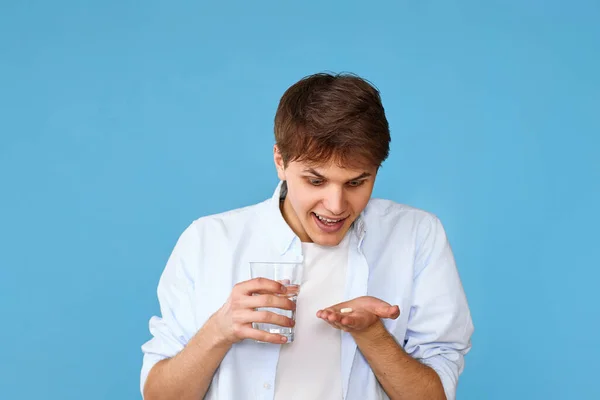 年轻英俊的男子拿着药丸和蓝色背景的杯子水 治疗概念 — 图库照片