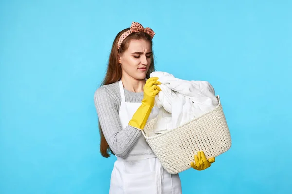 汚れた服を着たまま洗濯籠を持っている不幸な若い主婦青の背景 — ストック写真
