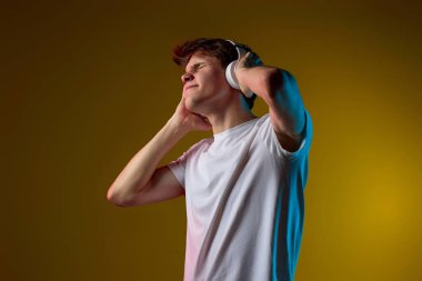 Kulaklıklı genç adam sarı arka planda en sevdiği müziğin keyfini çıkarıyor. Neon ışıkları