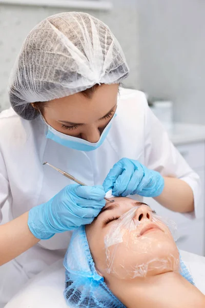 stock image young woman during a mechanical face cleansing procedure at beauty clinic. Cosmetologist making procedure for cleaning skin with steel tool from blackheads and acne