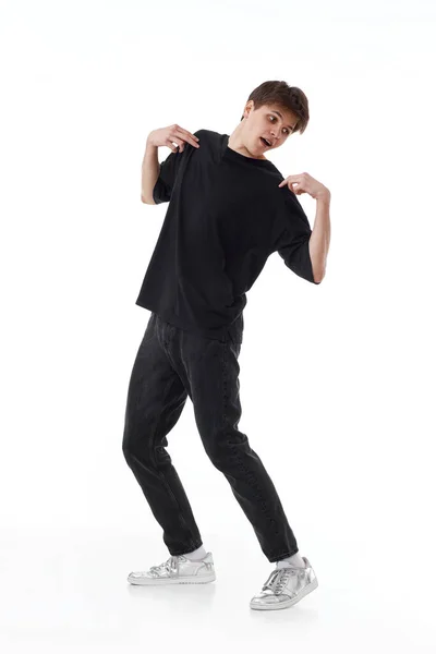 黒のTシャツとジーンズを着た若い興奮した男が白い背景で踊っている — ストック写真
