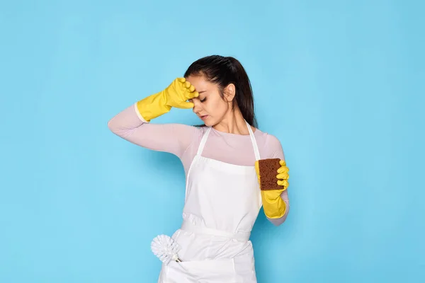tired woman gloves and cleaner apron with sponge on blue background