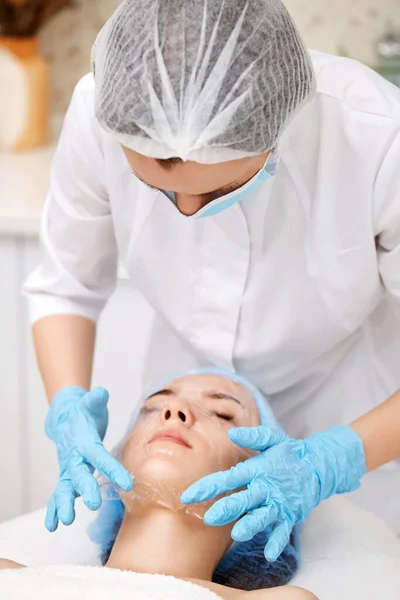 美容师在温泉沙龙的漂亮女人的脸上涂上薄片面罩 温泉治疗 — 图库照片