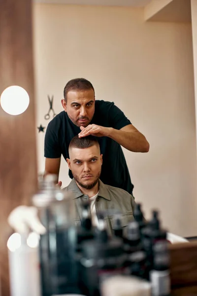 Barber and satisfied bearded man in front of the mirror in barber shop