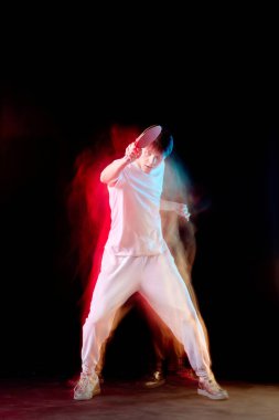 Genç adam karanlık arka planda karışık neon ışıkta masa tenisi oynuyor. Hareket kavramı