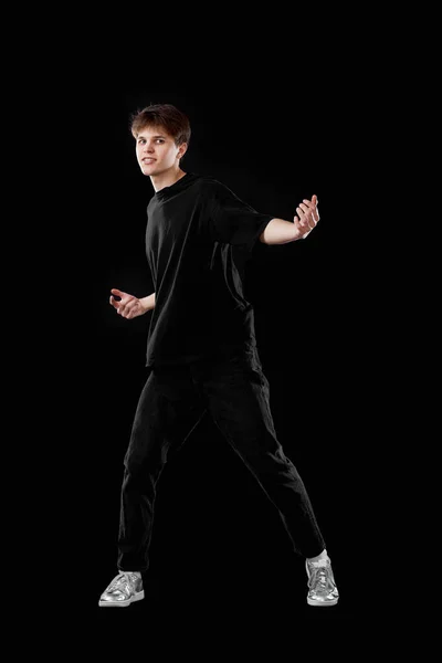 young man in black t-shirt dancing on black background. Full length