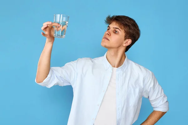 年轻英俊的男子 喝着一杯水 带着蓝色背景的快乐微笑 — 图库照片