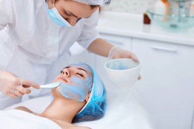 Güzellik uzmanı kaplıcadaki güzel kadının yüzüne mavi aljinat maske takıyor. spa tedavileri