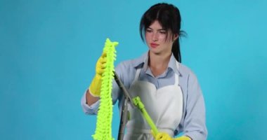 Profesyonel temizlikçi kız lastik eldivenli ve temiz önlüklü. Mavi arka plandaki plastik zemine yeşil bir bez koydu..