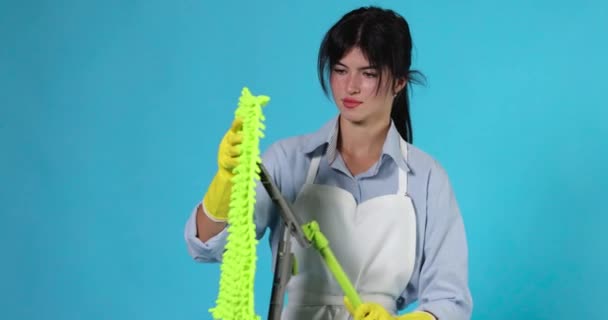 穿着橡胶手套和清洁围裙的专业清洁女工在蓝色背景的塑料地板拖把上铺上绿色抹布 — 图库视频影像