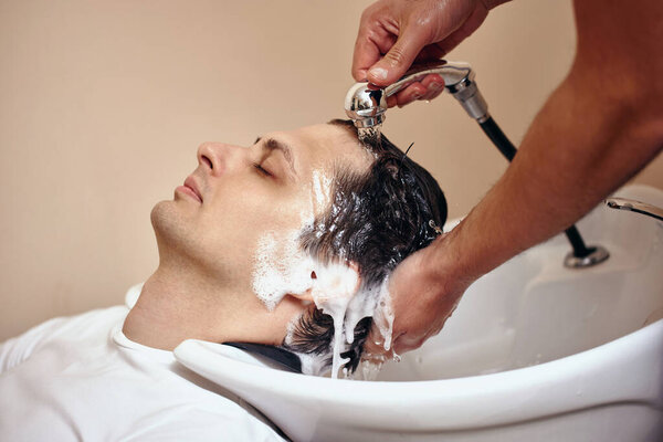 Парикмахер моет волосы кавказцу в парикмахерской