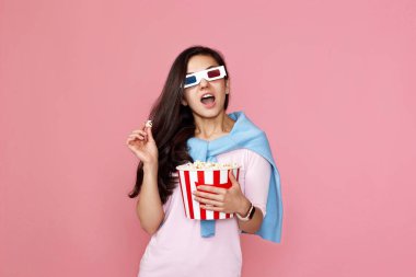 Korku filmi izleyen hayret bir kadın elinde pembe arka planda izole edilmiş patlamış mısır kovası tutuyor.