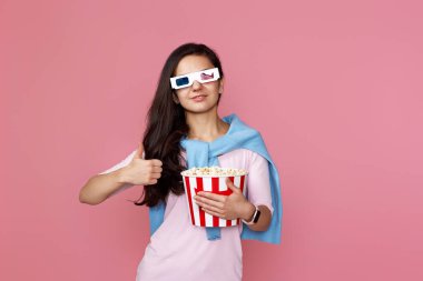 Şapkalı neşeli genç kadın, elinde patlamış mısırla pembe arka planda 