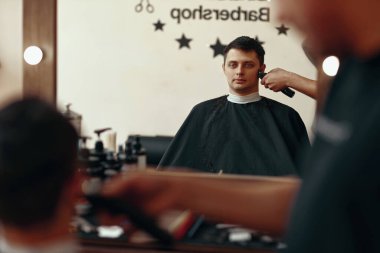 Berber dükkanındaki yakışıklı beyaz adamın saçlarını elektrikli makasla kes..