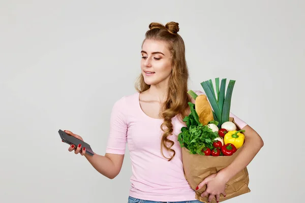 여자가 식료품들로 친화적 가방을 스튜디오 배경에 스마트폰을 사용하고 있습니다 — 스톡 사진