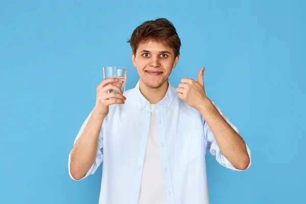 微笑友善的男人 喝了一杯水 在蓝色的背景上举着大拇指 — 图库照片