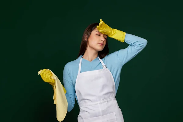 tired woman in yellow gloves and cleaner apron on green background