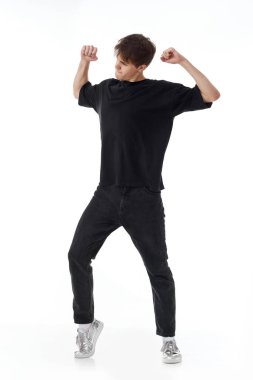 Beyaz arka planda dans eden siyah tişörtlü ve kot pantolonlu genç keyifli bir adam. Tam uzunluk