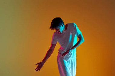 Yakışıklı genç adam neon ışıklarıyla sarı arka planda neşe içinde hareket ediyor.