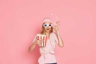 Kısa saçlı, korku filmi izleyen, elinde pembe arka planda bir kova patlamış mısır tutan korkmuş bir kız.