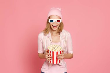 Çok heyecanlı genç sarışın kadın elinde patlamış mısırla pastel pembe arka planda