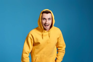 Mavi arka planda sarı tişörtlü yakışıklı adam şaşırdı.