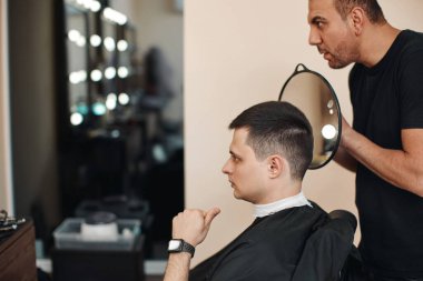 Berber dükkanında aynanın önünde sakallı ve tatmin olmuş bir adam.