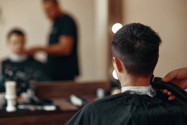 Rear view of barber shaving handsome caucasian man in barber shop. clipart