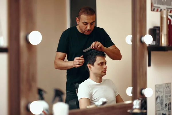 Professional hairdresser and client man in front of the mirror in barber shop. Haircut in the barbershop.