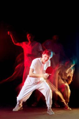 Koyu arkaplanda karışık neon ışıkta masa tenisi oynayan beyaz bir adam. Hareket kavramı