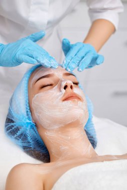 Güzellik uzmanı maskeyi güzellik salonundaki güzel genç bayanın yüzüne takıyor. yüz bakımı konsepti.