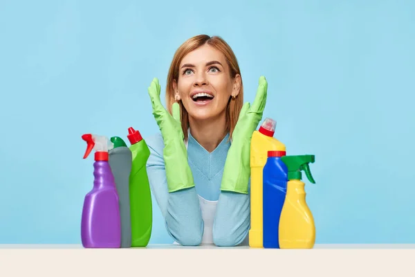 blonde young woman with cleaning agents on table on blue background