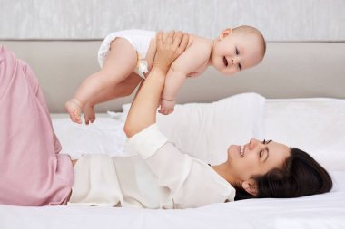 Gülümseyen anne yeni doğmuş bebeğini havaya kaldırıyor. Mutlu aile.