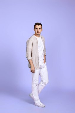 Pastel mor arka planda poz veren günlük beyaz giysili beyaz bir adam. Tam boy fotoğraf