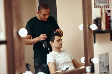 Berber dükkanında aynanın önünde duran berber ve beyaz adam.