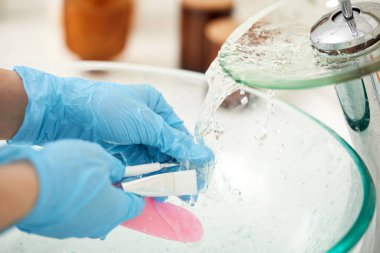 Mavi eldivenli kadın elleri kozmetik spatulasını yıkıyor.