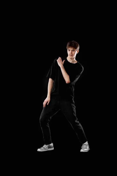 excited young man in black t-shirt dancing on black background. Full length