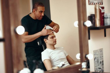 Berber dükkanında aynanın önünde duran berber ve beyaz adam.